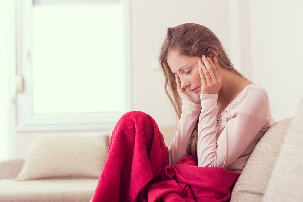 Tension headaches hurt woman as she sits on the couch